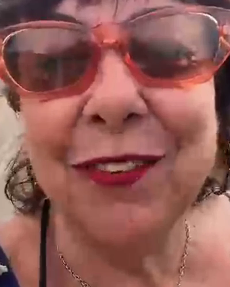 Rachel sorrindo com batom vermelho, ao ar livre
